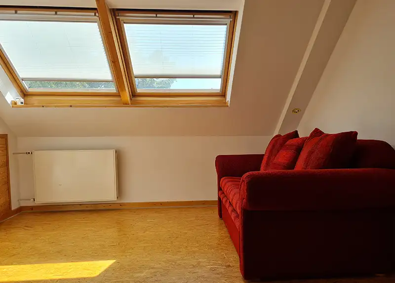Leeres Dachgeschoss mit rotem Sofa und Dachfenstern